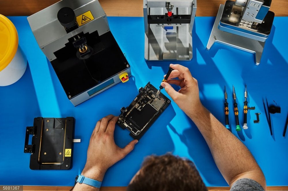 Portaltic.-Apple modifica su programa de reparación para admitir piezas procedentes de iPhone usados Técnico sobre una mesa con piezas y herramientas reparando un iPhone
